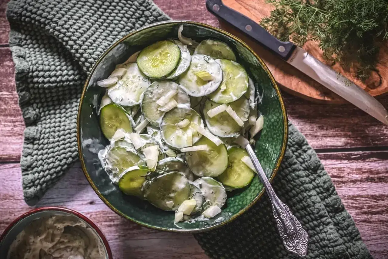 Frischer gurkensalat mit schmand und Dill, garniert mit Zwiebeln, serviert in einer gr&uuml;nen Sch&uuml;ssel.