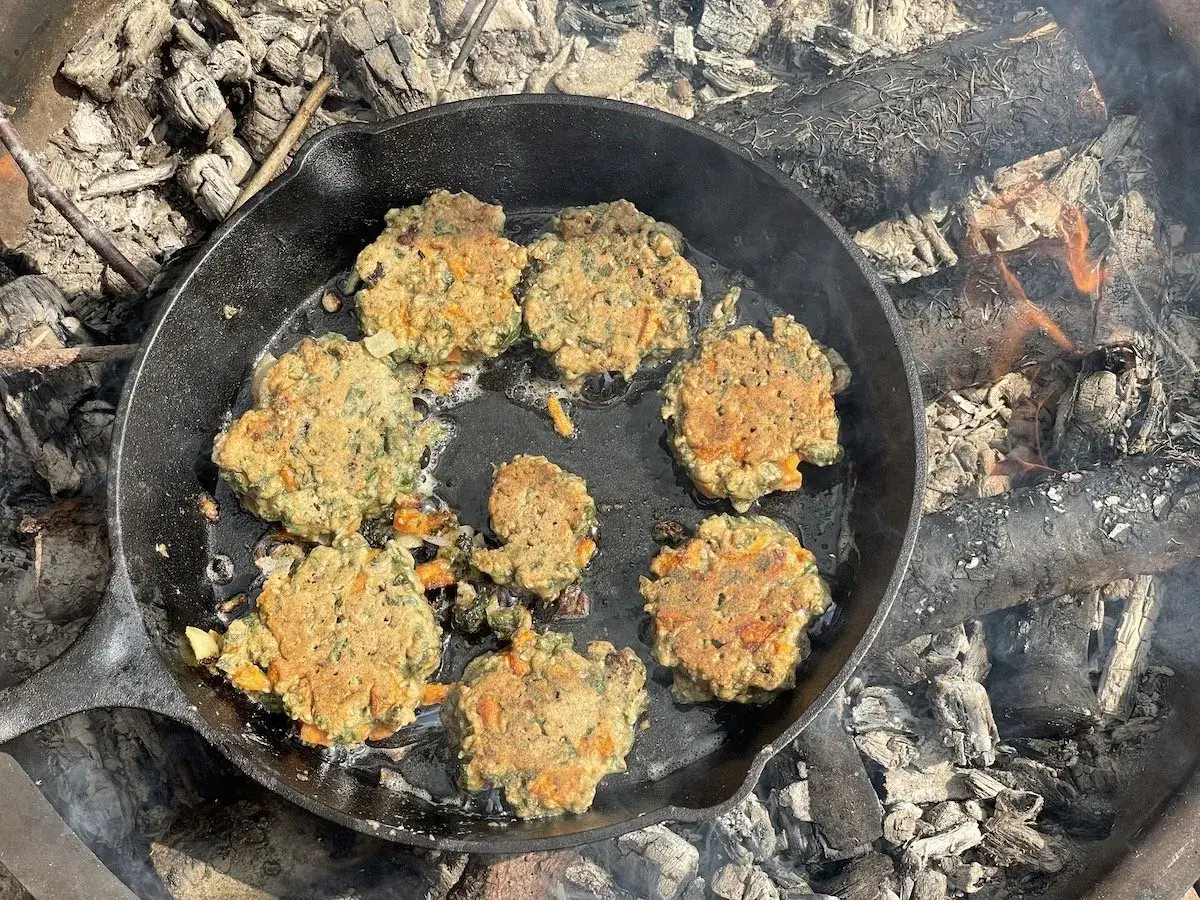 Kleine Bratlinge aus Brennnesseln und Karotten brutzeln in einer Gusseisenpfanne über einem Lagerfeuer. Lecker, wenn man Brennnesseln essen möchte!
