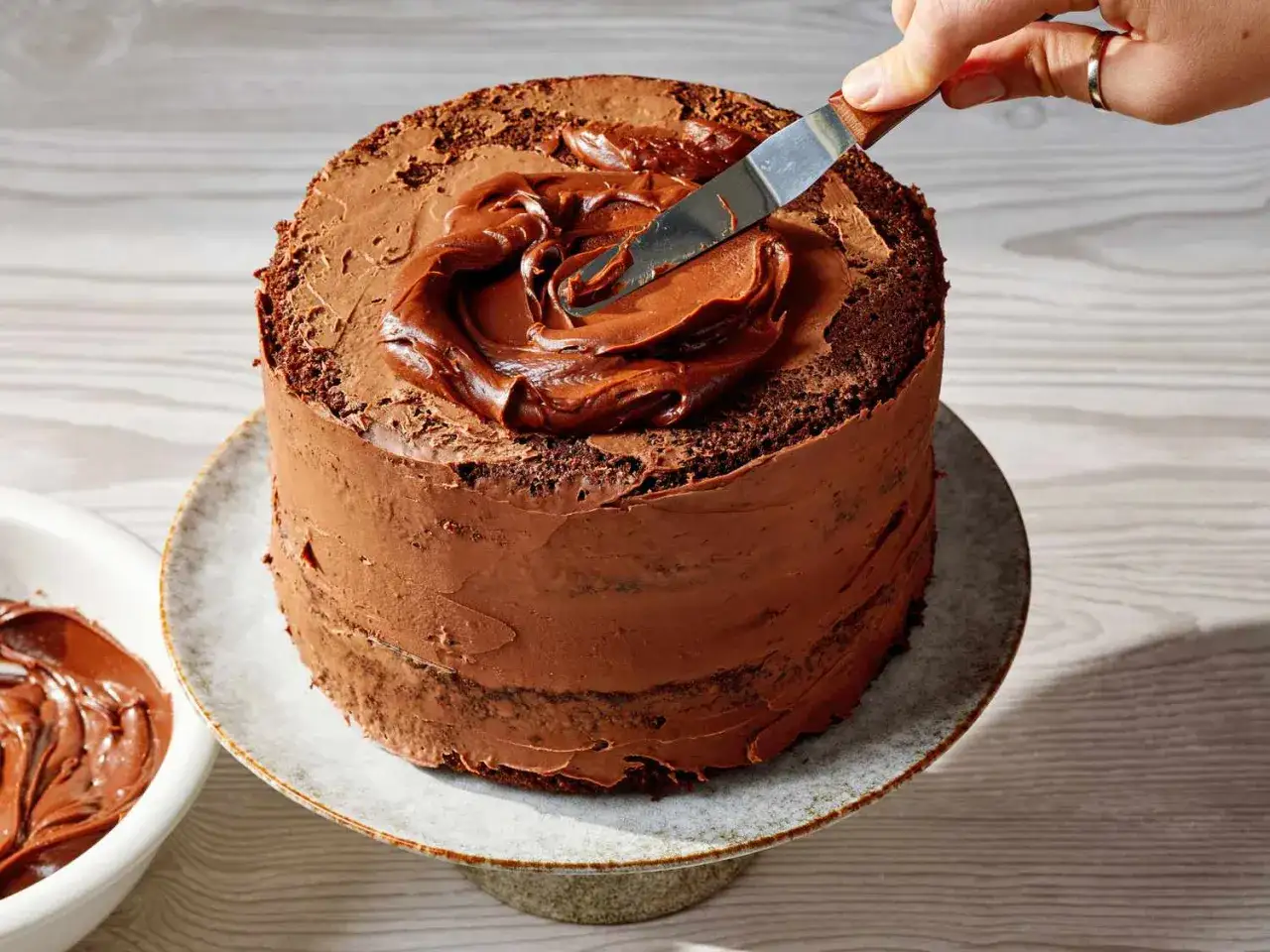 Schokoladenkuchen wird mit einer glatten Glasur überzogen. Mit einem Spachtel wird die Glasur auf dem Kuchen verteilt, um das Glasur selber machen zu perfektionieren.