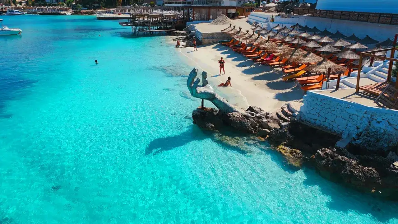 En vacker albanien strand med turkost vatten, solstolar och en unik handstaty.