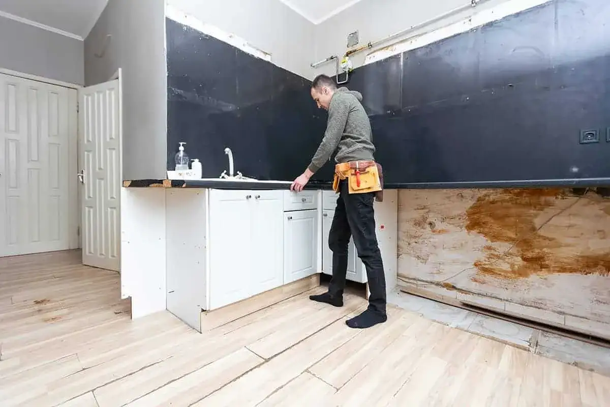 Remont kuchni od czego zacząć? Mężczyzna w pasie narzędziowym sprawdza szafki pod zlewem.