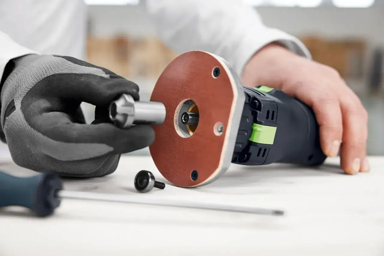 Main d'un artisan ajustant un accessoire sur une défonceuse Festool OFK 500.