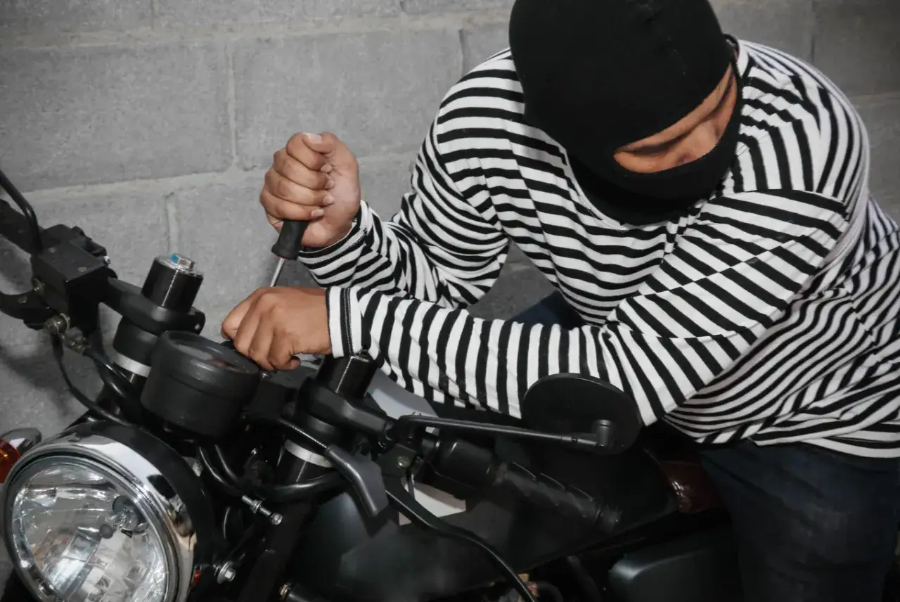 Złodziej w masce próbuje ukraść motocykl, używając śrubokręta. To pokazuje, jak ważne jest zabezpieczenie motocykla przed kradzieżą.