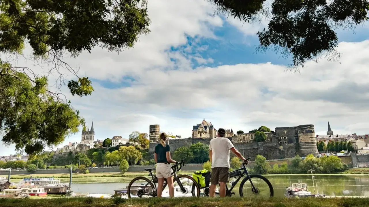 Couple with bikes enjoying a scenic view of a castle and river, perfect for Loire Valley cycling tours.