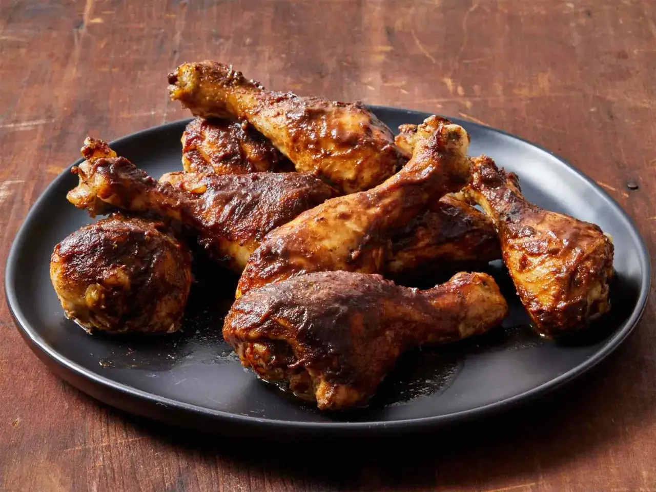 Une assiette de pilons de poulet grill&eacute;s, brillants d'une sauce savoureuse, sur fond de bois sombre.