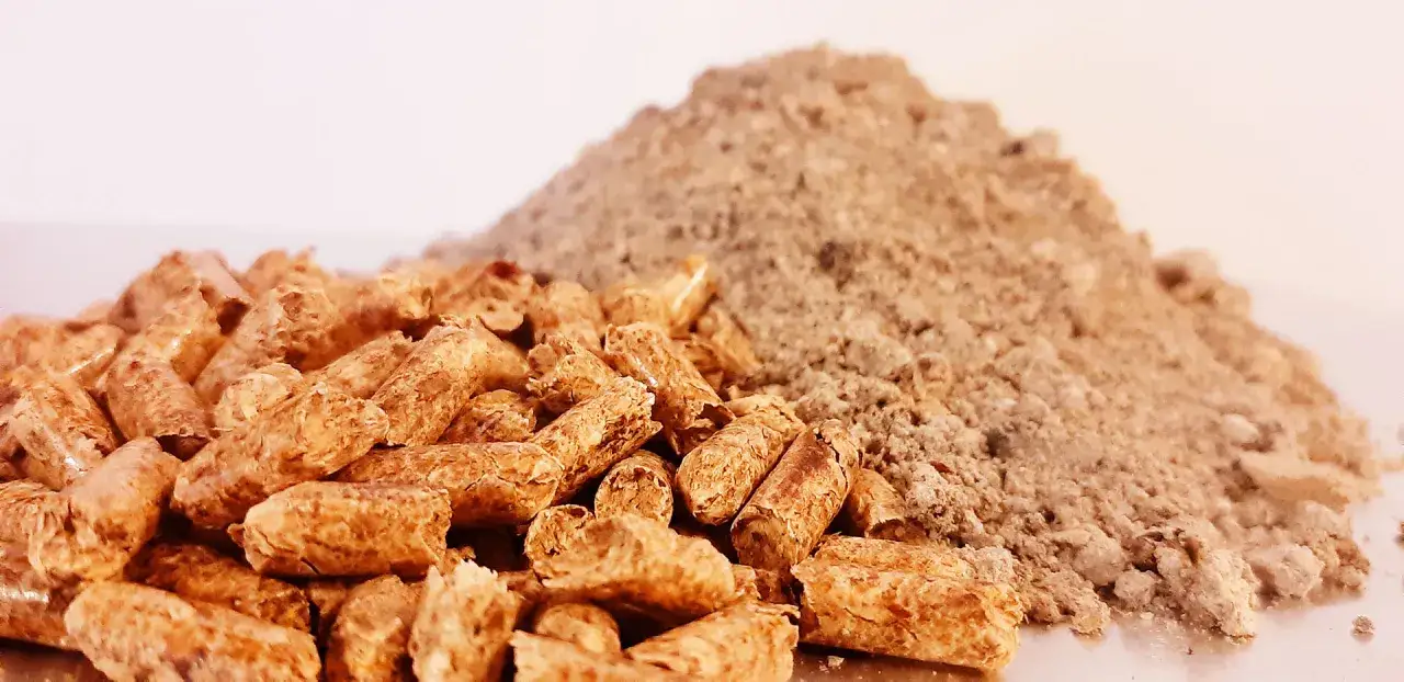 Un mucchio di pellet di paglia per stufe, combustibile ecologico, accanto a una pila di polvere fine.