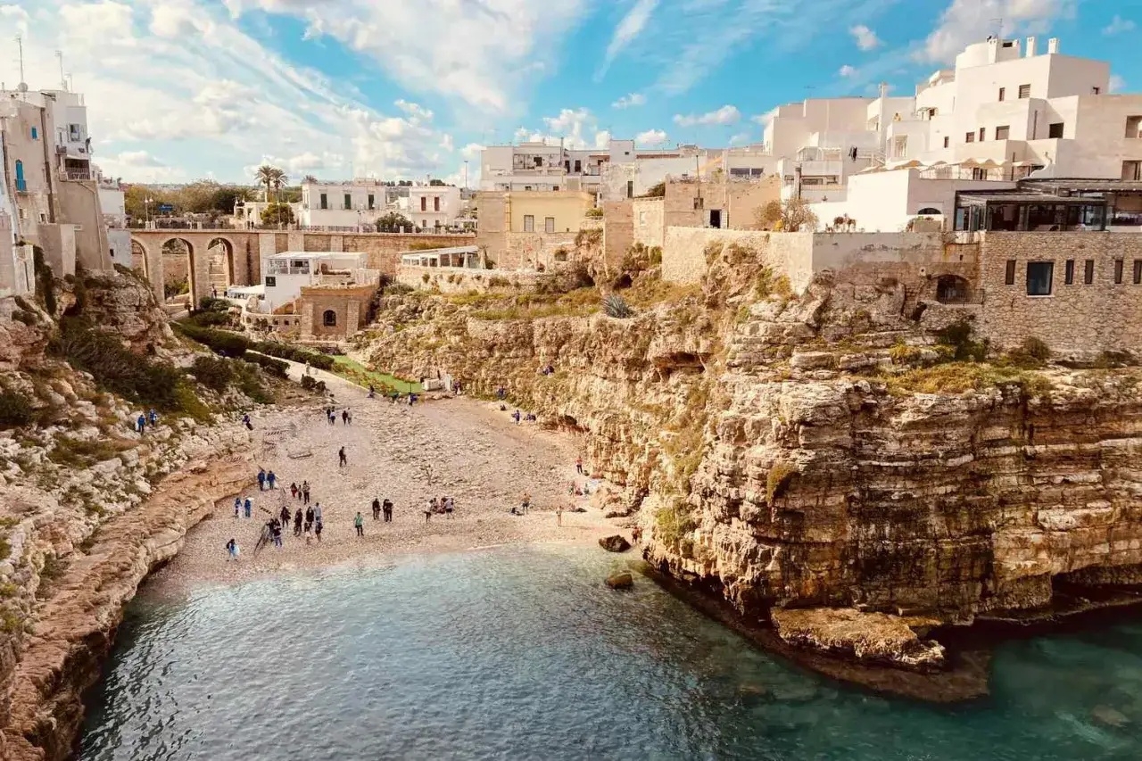 Un'incantevole spiaggia di ciottoli a Polignano a Mare, con case bianche arroccate sulle scogliere. Un perfetto scorcio di puglia estate.