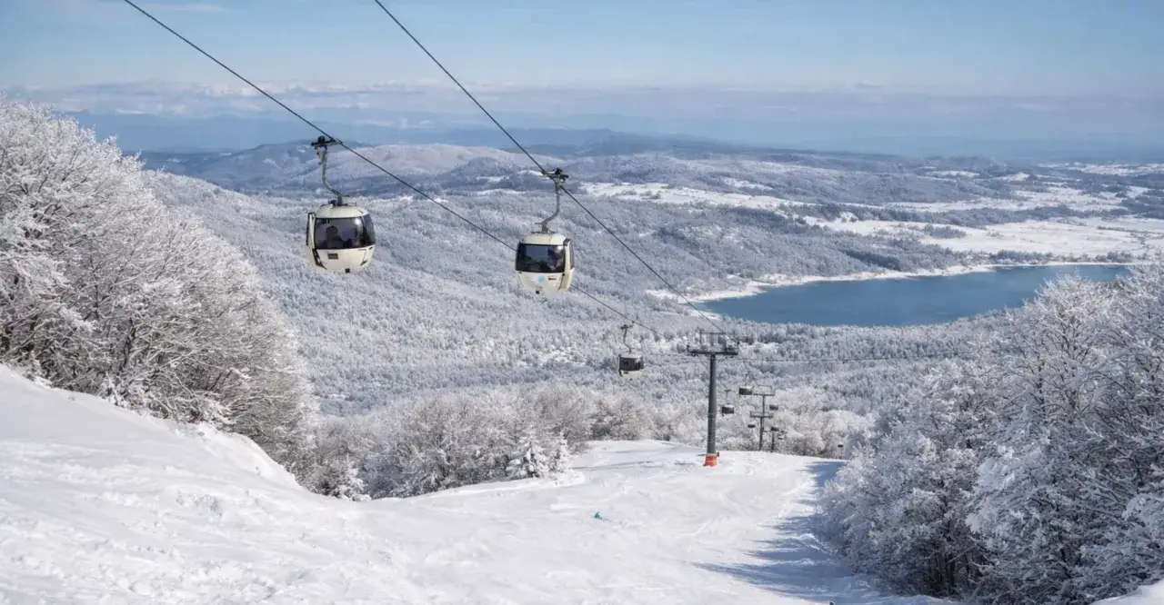 Immagini mozzafiato per scoprire dove sciare in Calabria: cabinovie su un paesaggio innevato con lago sullo sfondo.
