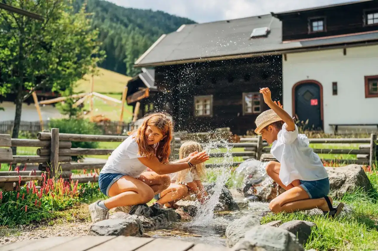 Trois enfants s'amusent dans un ruisseau, éclaboussant joyeusement. Parfaites vacances scolaires en Autriche pour se rafraîchir !