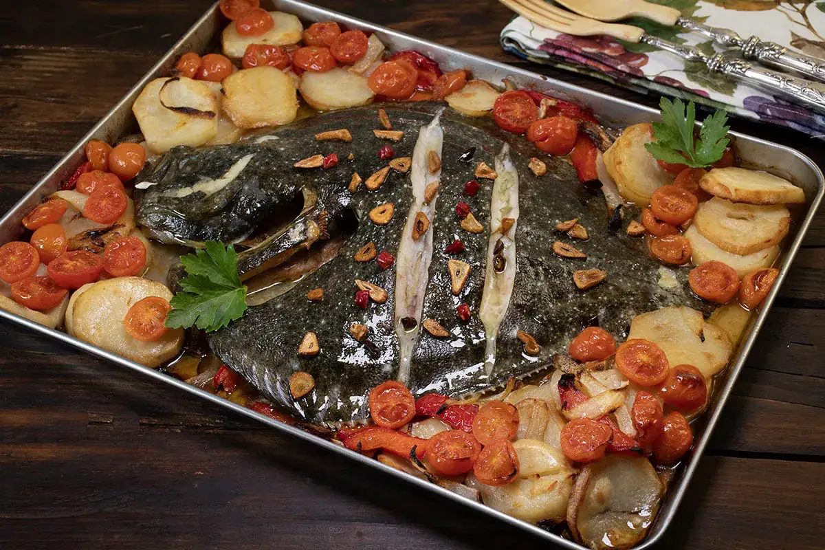 Rodaballo al horno con patatas, tomates cherry y ajo laminado. Un plato jugoso y lleno de sabor.
