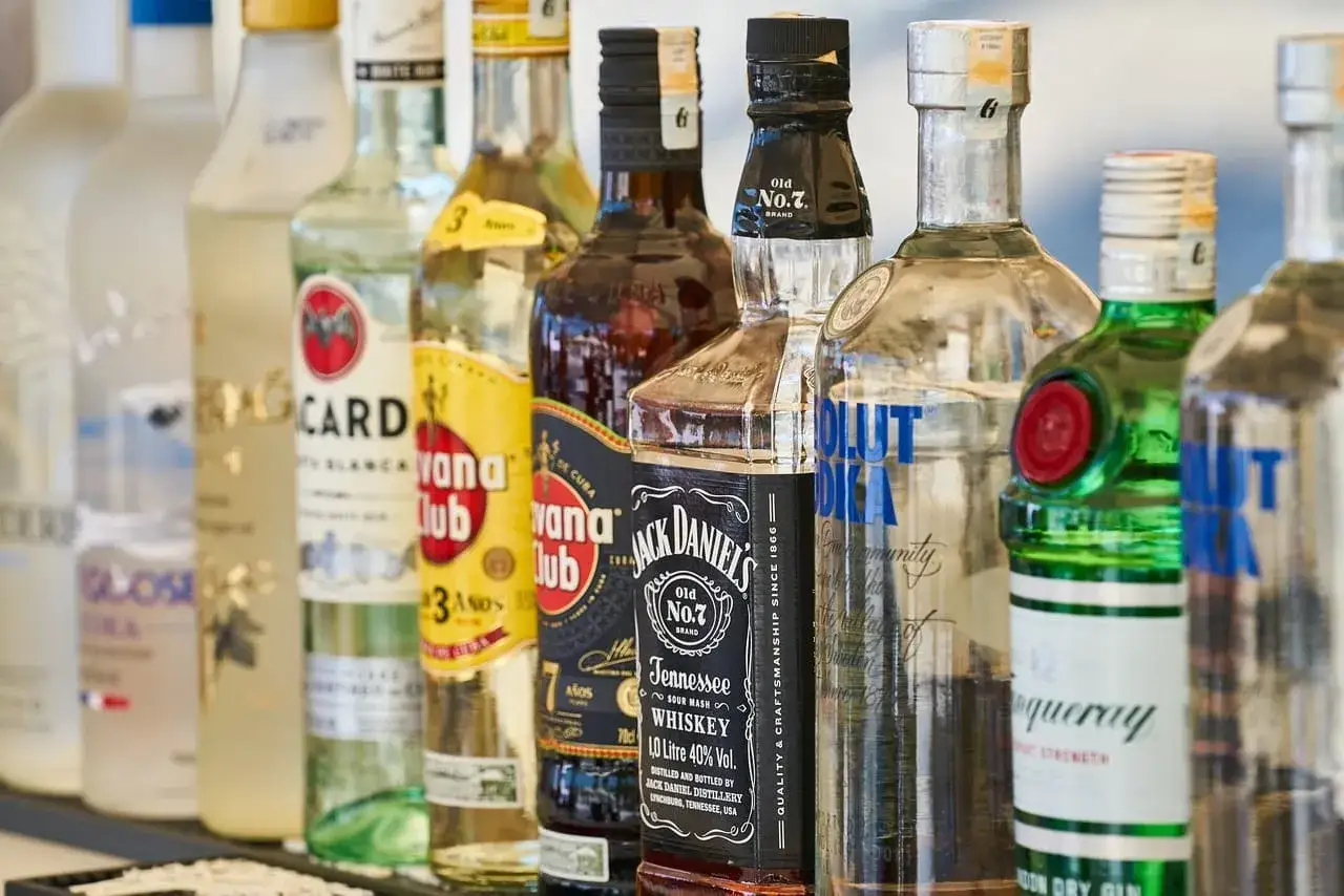 Rząd butelek alkoholi: wódka, rum, whisky. Czy wódka ma datę ważności? Te butelki wyglądają na długowieczne.