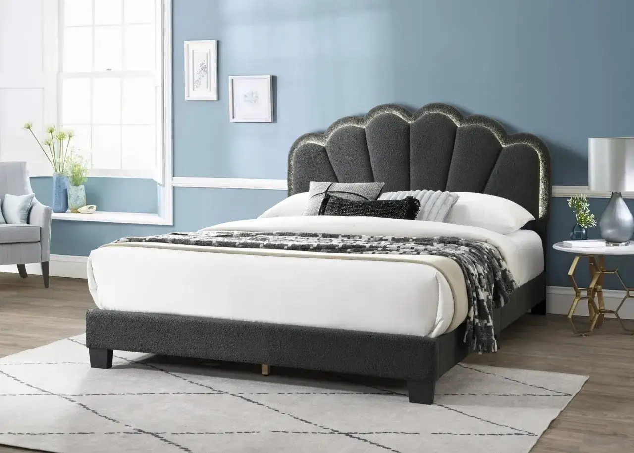 Stilvolles Schlafzimmer mit grauem Boxspringbett, das mit einer Muschel-f&ouml;rmigen, beleuchteten Kopfst&uuml;tze und einem gemusterten &Uuml;berwurf dekoriert ist.