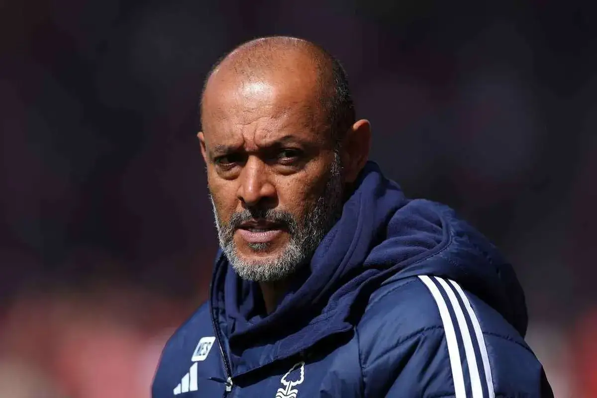 Skupiony nottingham forest trener w niebieskiej kurtce z białymi paskami, z siwą brodą i łysą głową.