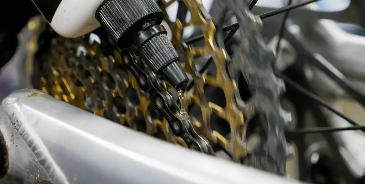 Lubricating the mtb drivetrain. A drop of oil falls onto the chain, ready to glide over the golden cassette.