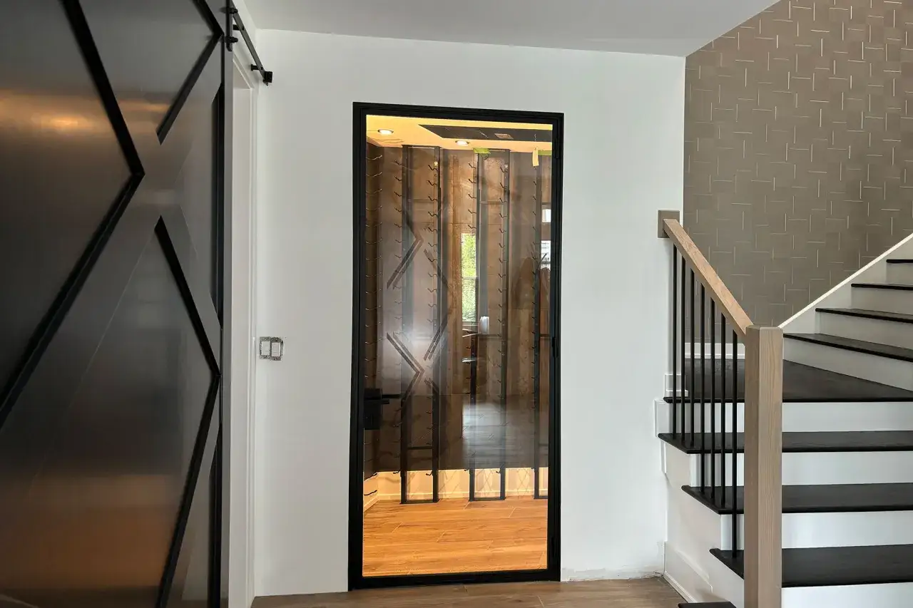 Une porte vitrée avec un encadrement de porte couleur différente, menant à une cave à vin. À côté, un escalier moderne et une porte coulissante noire.