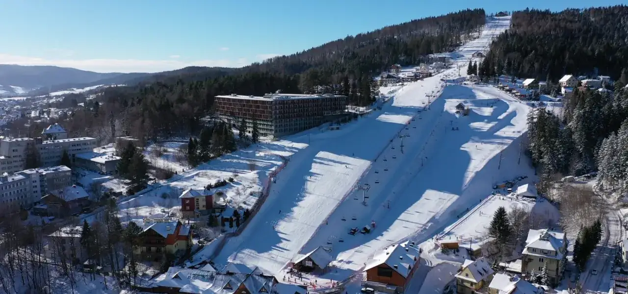 Idealne miejsce, gdzie pojechać na ferie zimowe w Polsce: stok narciarski z wyciągami, hotel i urokliwe domki w śnieżnej scenerii.