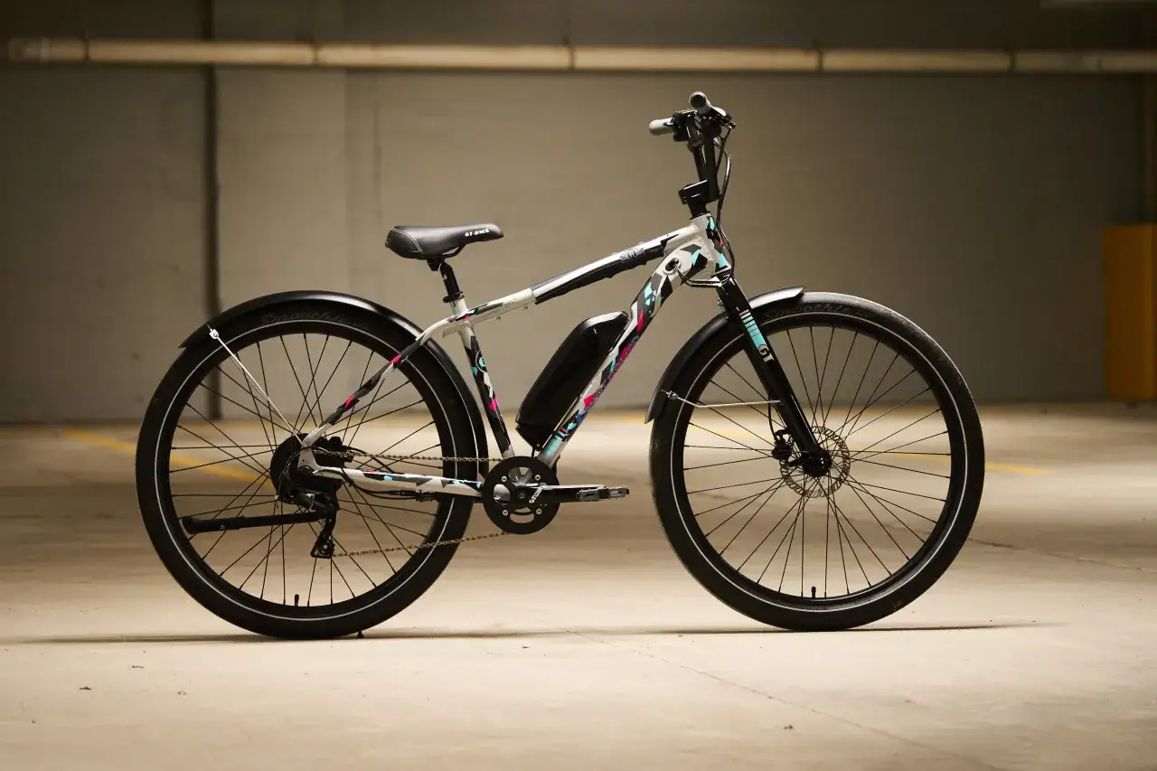 A white electric bike with colorful geometric accents, featuring a black battery pack and fenders. This GT power performer is ready for any adventure.