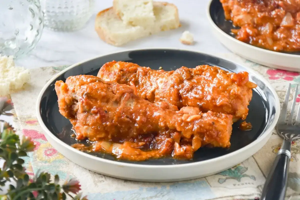Jamoncitos de pollo en salsa, servidos en plato oscuro, acompa&ntilde;ados de pan y tenedor.