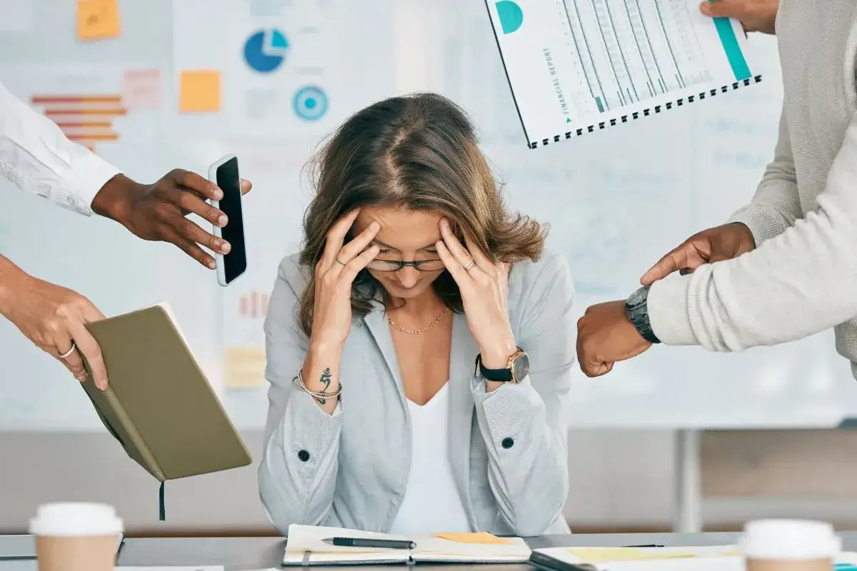 Donna sopraffatta da richieste lavorative, simile a chi vive con **ADHD adulti testimonianze**. Mani che porgono telefono, report e agenda.