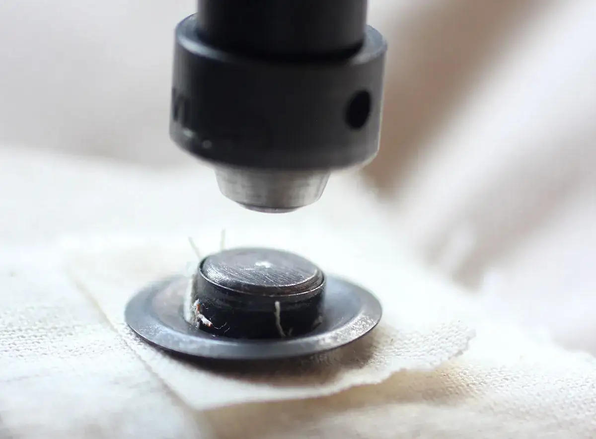 Close-up of a tool pressing metal rings into fabric, demonstrating how to put metal rings in fabric for a secure finish.