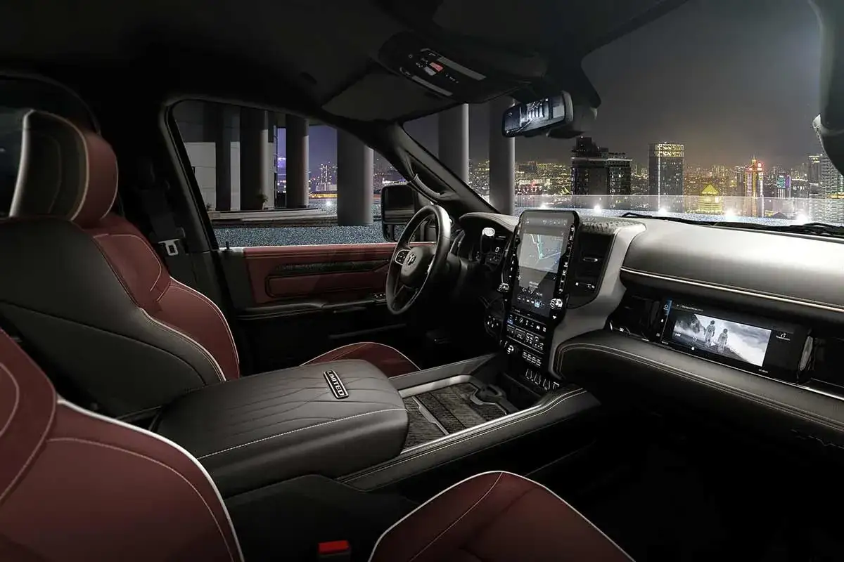 Luksusowe wnętrze Dodge Ram 3500 z bordowo-czarnymi skórzanymi fotelami i nowoczesnym panelem multimedialnym, nocą z widokiem na miasto.