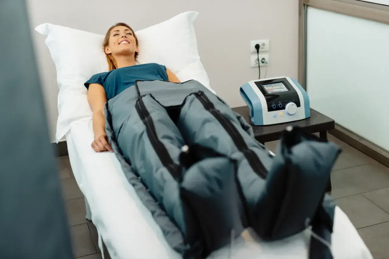 Uśmiechnięta kobieta w specjalnych nogawkach do presoterapii. Pamiętaj o **presoterapia przeciwwskazania** przed zabiegiem.