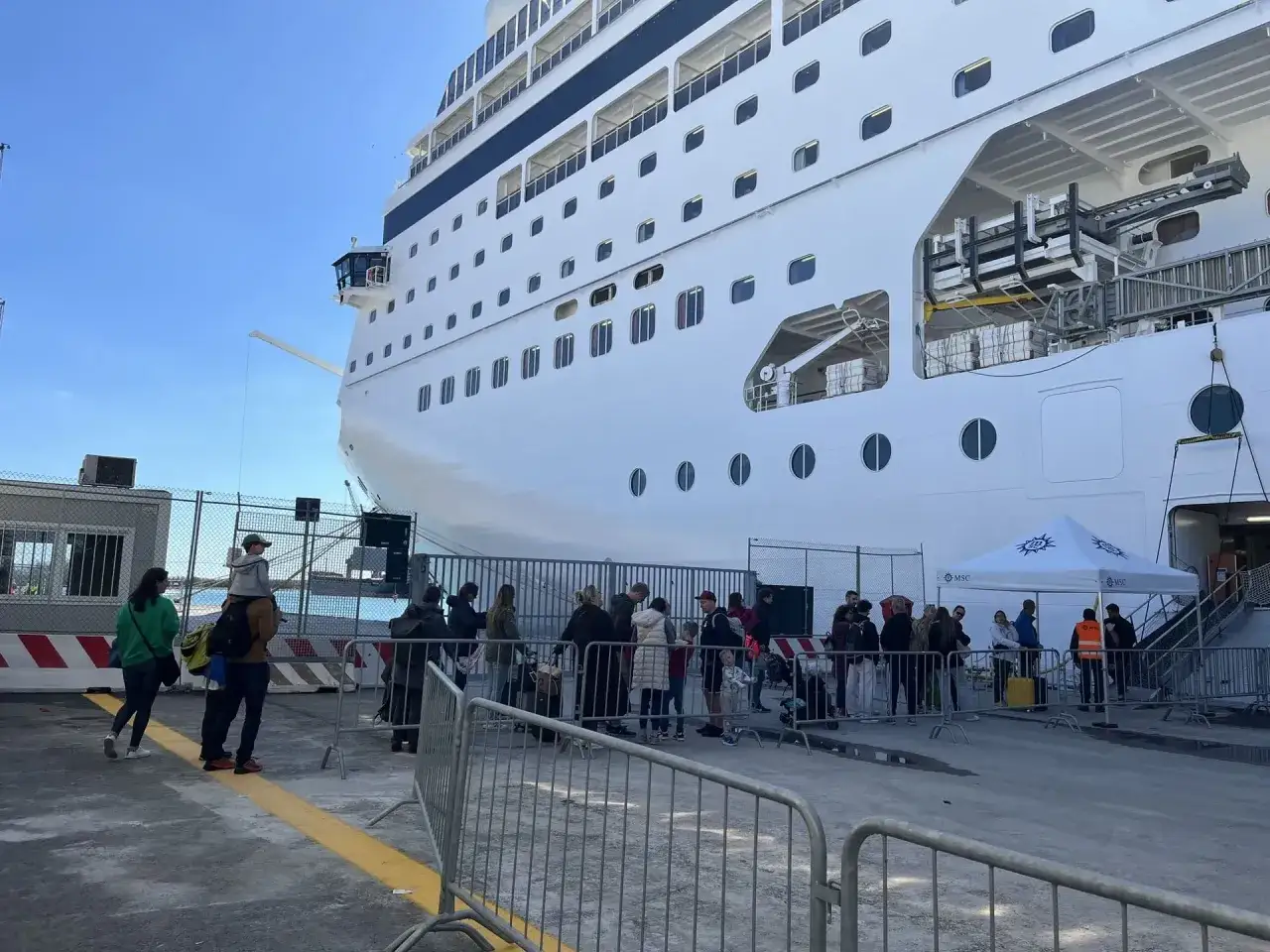 Persone in fila per l'imbarco crociera, chiedendosi quanto tempo prima arrivare. La nave bianca è imponente.
