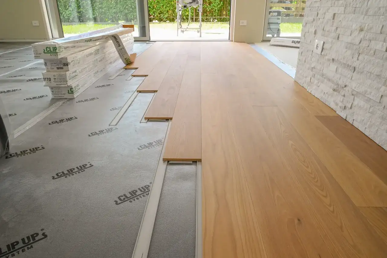 Installazione di parquet incollato su un sottofondo preparato. Le assi di legno chiaro sono disposte in file ordinate, pronte per essere fissate.