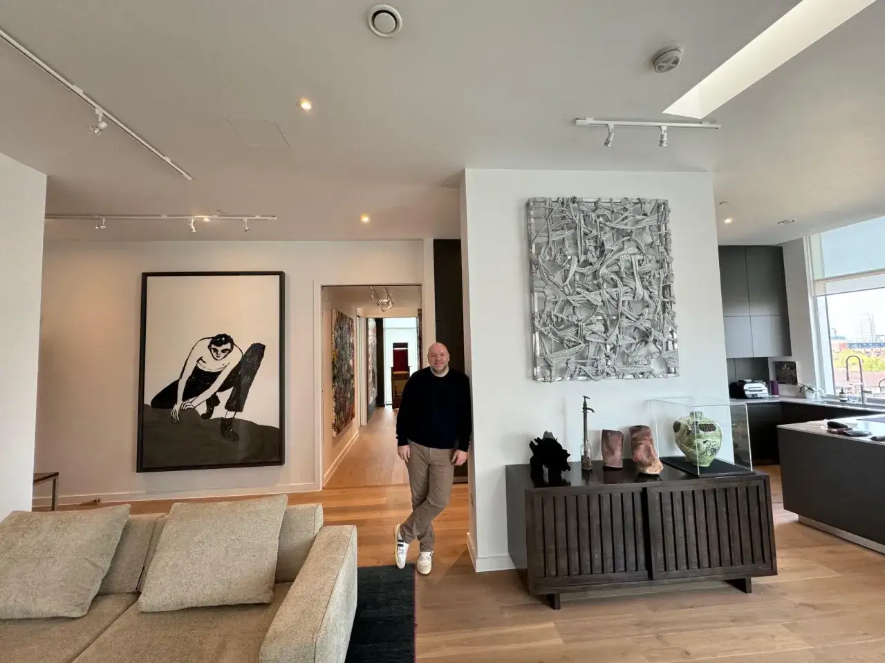 A man stands in a modern living room filled with art, showcasing his discerning taste in art investment.