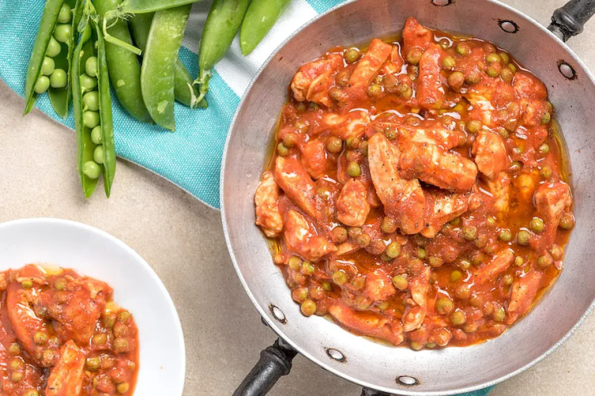 Delizioso petto di pollo con piselli in salsa rossa, servito in padella e in una ciotola, con piselli freschi ancora nel baccello sullo sfondo.