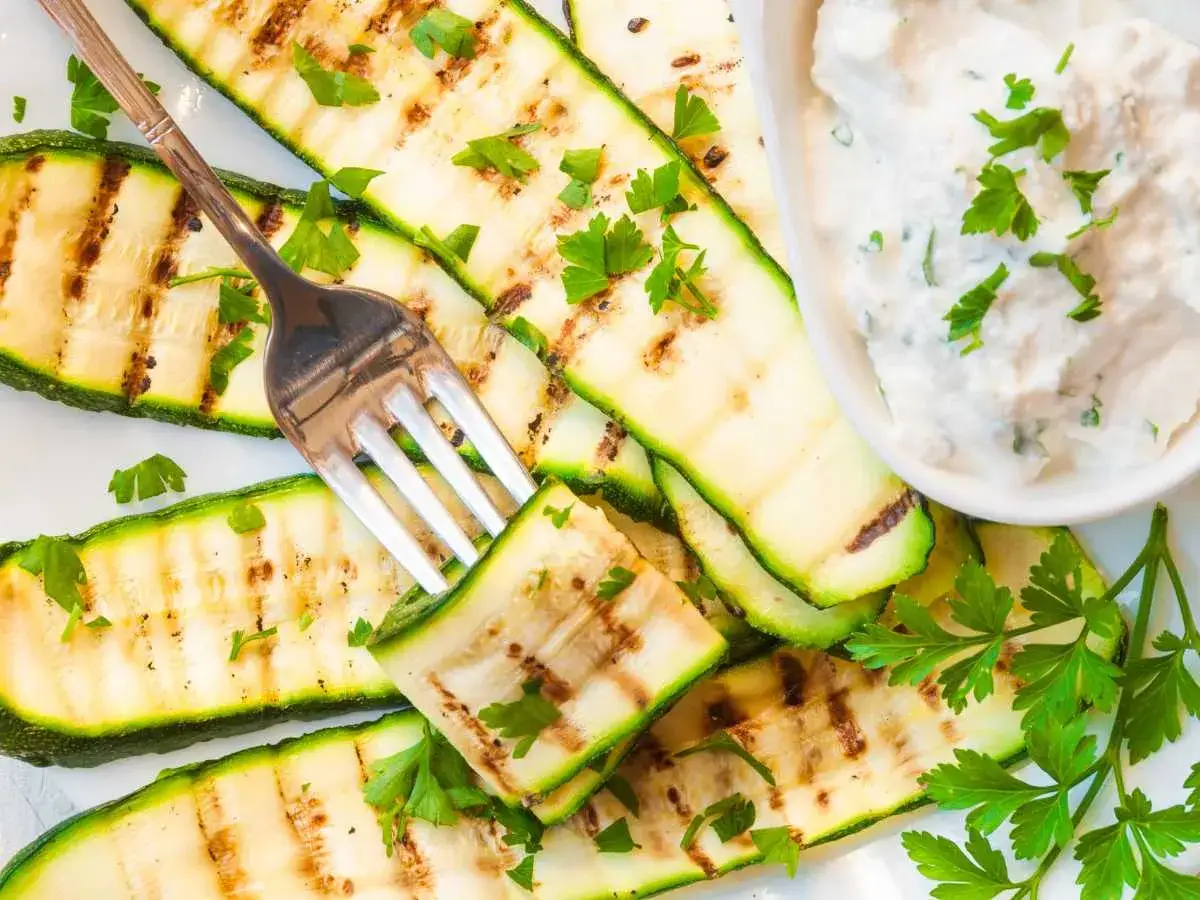 Calabacín a la plancha con hierbas frescas y una cremosa salsa de yogur. Un tenedor listo para probar esta delicia.