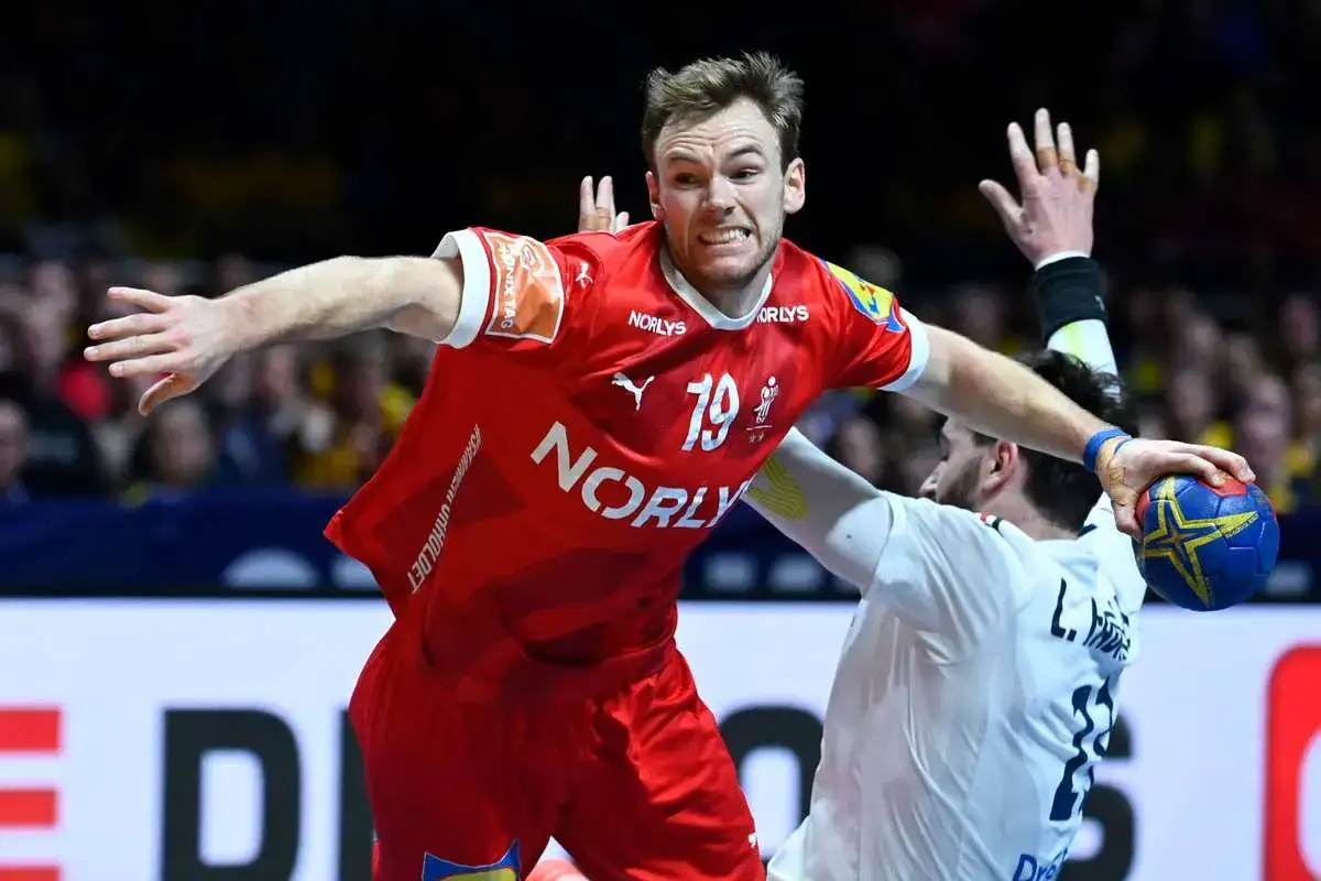 Mathias Gidsel w czerwonej koszulce z numerem 19, w akcji podczas meczu piłki ręcznej, walczy o piłkę z przeciwnikiem.