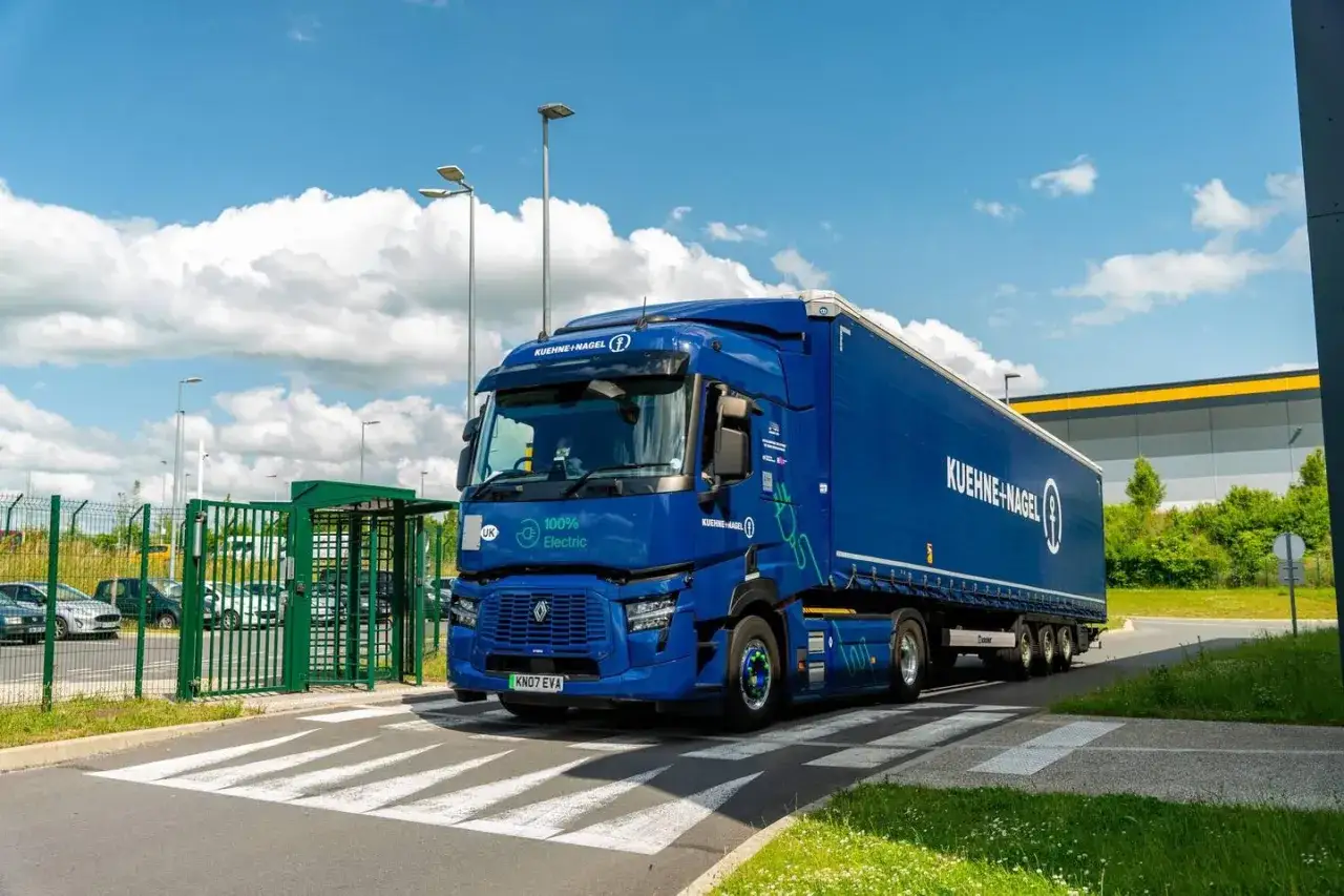 Niebieska ciężarówka elektryczna Kuehne+Nagel wjeżdża na teren. Zastanawiasz się, ile kosztuje prom do Anglii z samochodem?
