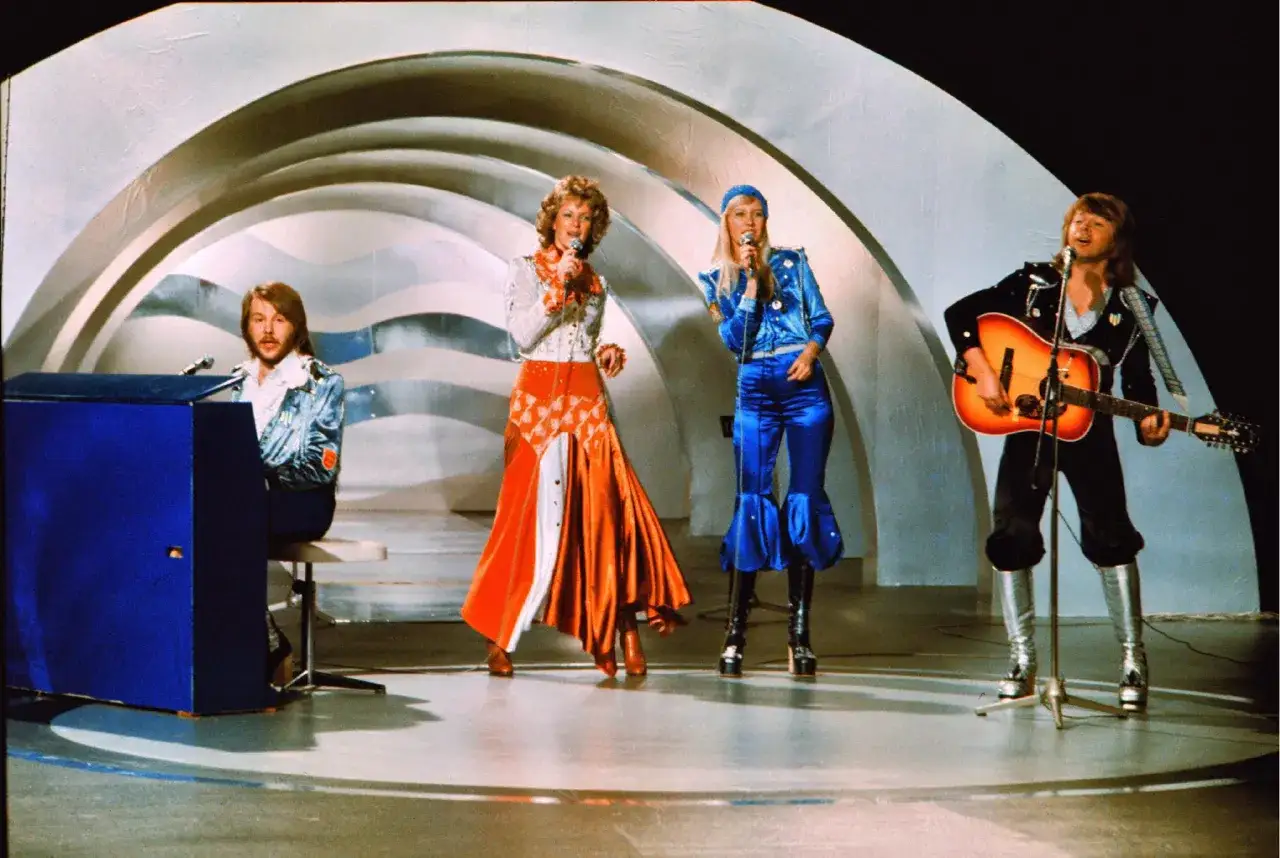 Zespół ABBA na scenie, wykonujący swoje piosenki. Agnieszka śpiewa, Björn gra na gitarze, a Benny na pianinie.