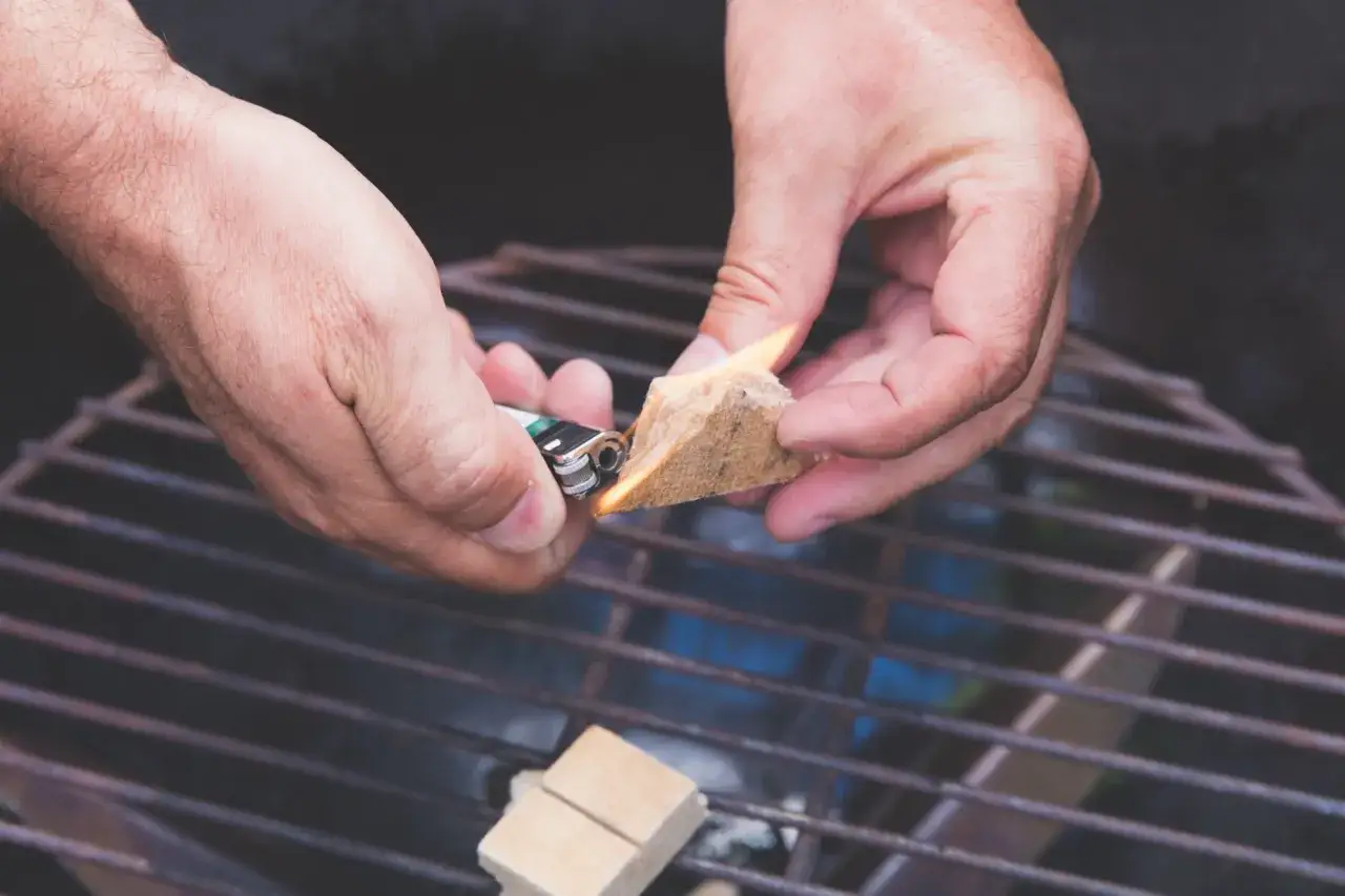 Hände zünden Grillanzünder an, um den Grill anzuheizen. Bald gibt es leckeres Essen!