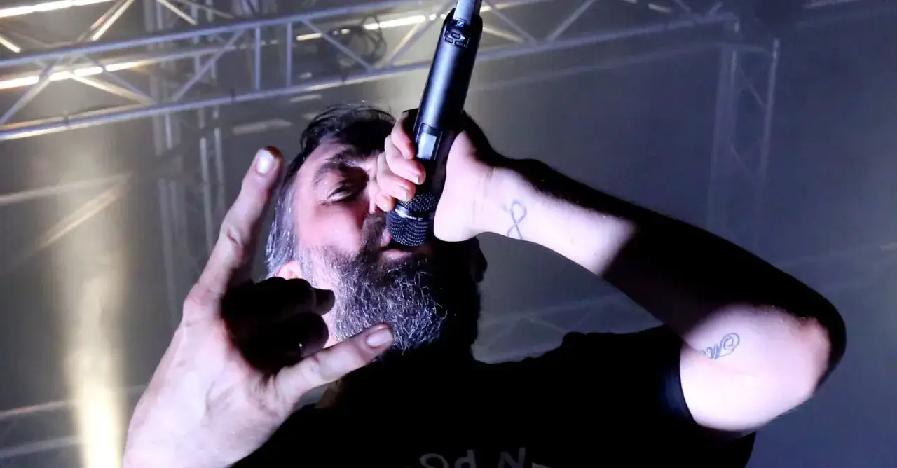 Le chanteur Mass Hysteria, micro en main, fait un signe de rock sur sc&egrave;ne.
