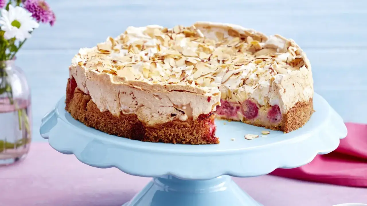Ein köstlicher Stachelbeer Baiser Kuchen mit Mandelsplittern und saftigen Früchten, präsentiert auf einem hellblauen Tortenständer.