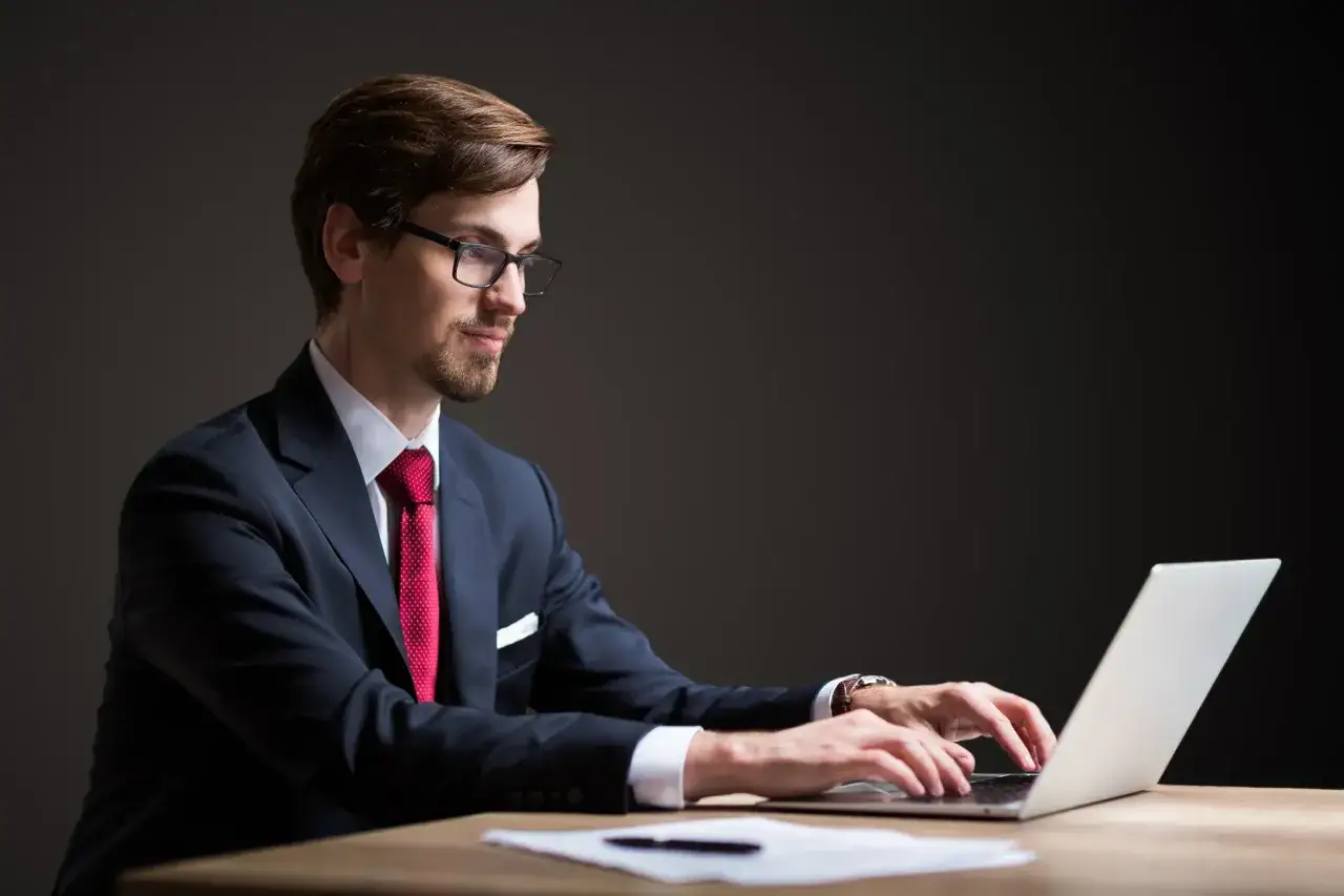 Mężczyzna w garniturze i okularach pracuje przy laptopie. To doskonały przykład pracy fotografa, który uchwycił profesjonalizm.