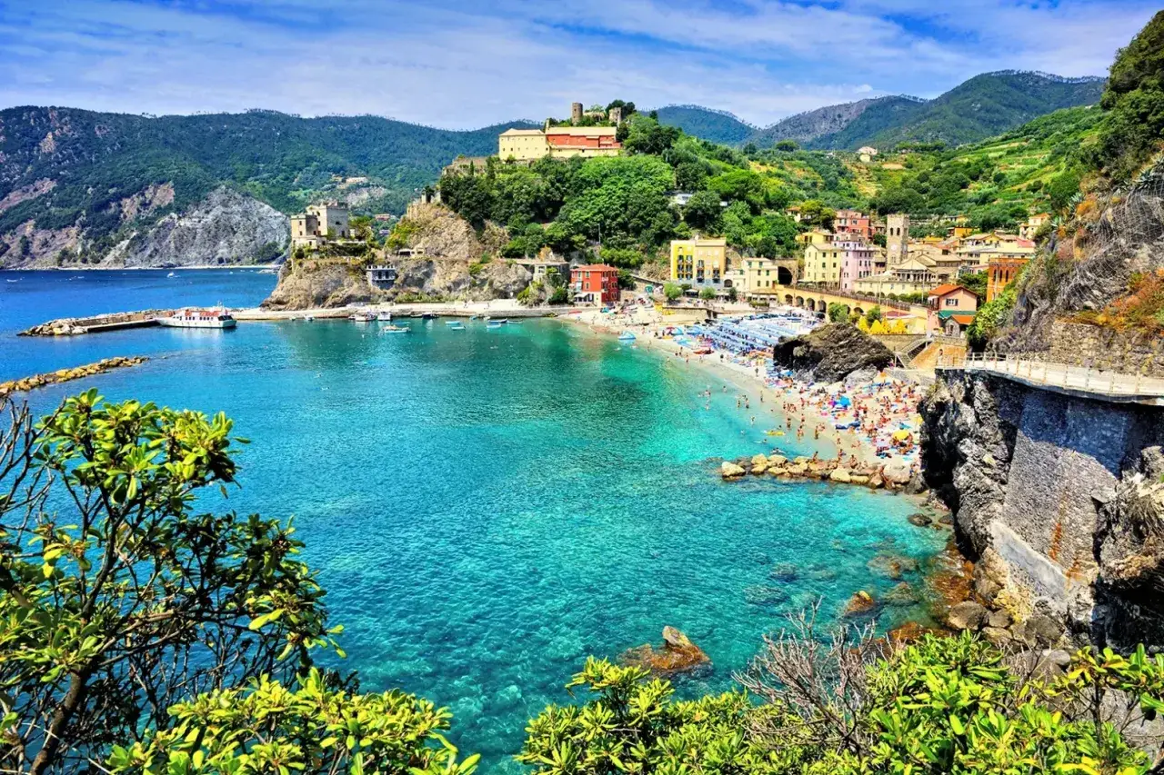Vue d'un gite Cinque Terre, avec une plage bondée, des eaux turquoise et des maisons colorées perchées sur la falaise.