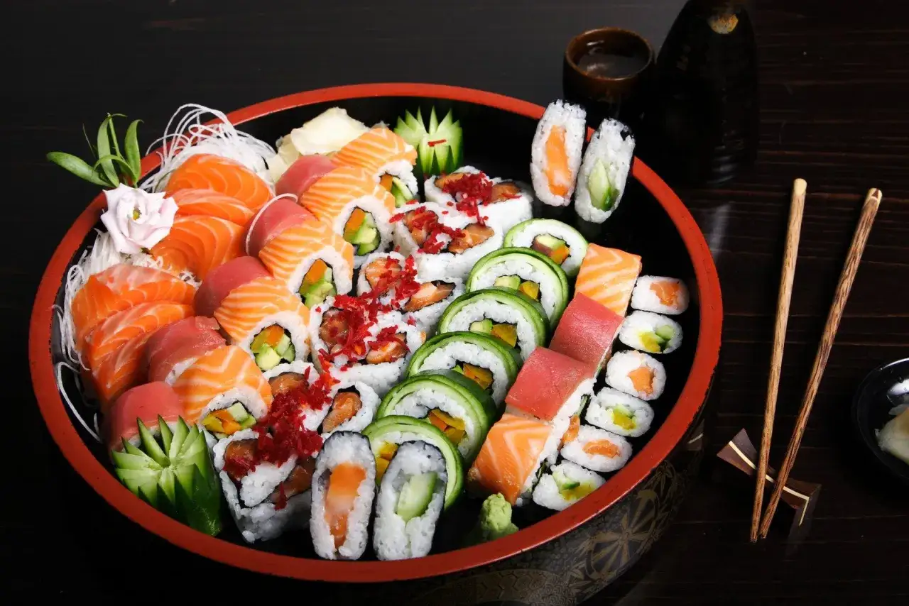 Talerz pełen r&oacute;żnorodnych sushi, w tym nigiri z łososiem i tuńczykiem, rolki z og&oacute;rkiem i awokado, a także kilka kawałk&oacute;w temaki sushi.