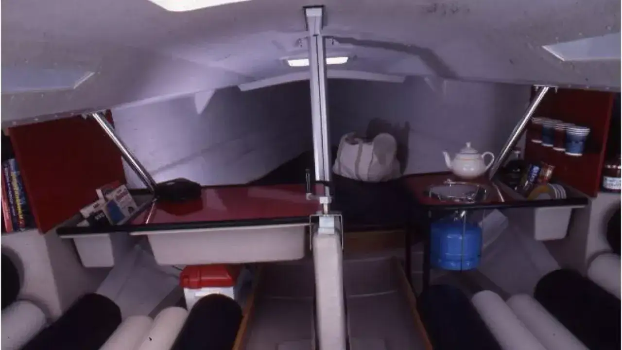 Intérieur d'un voilier First Class 8. Équipement de cuisine, vaisselle, et sacs de couchage prêts pour une aventure en mer.