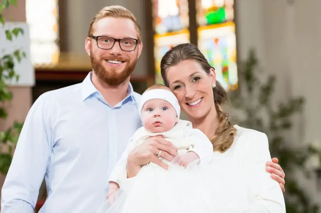 Un couple souriant pose avec leur bébé en tenue de baptême. Une belle raison pour accepter d'être parrain.