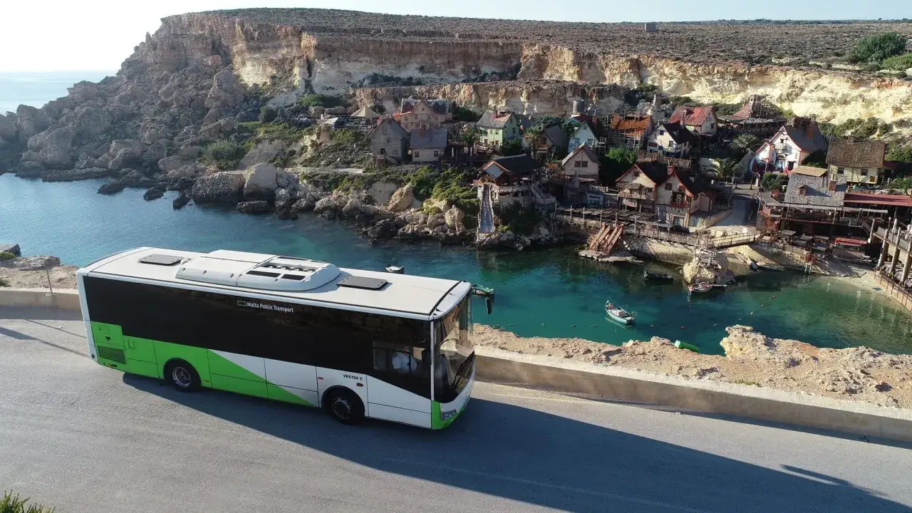 Autobus Malta Public Transport przy malowniczej zatoce z kolorowymi domkami w Popeye Village. Komunikacja na Malcie dociera wszędzie.