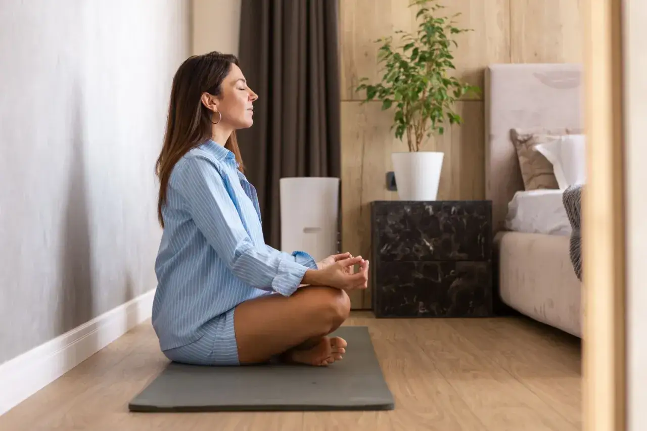 Kvinna med slutna ögon sitter i meditationsställning på en matta. Hon upplever lugn och ro, en av många meditation effekter.