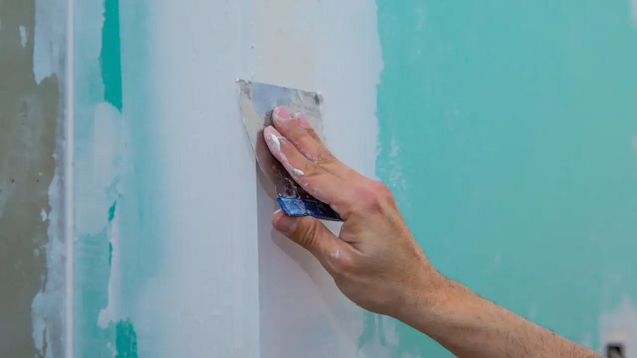 Hand spacklar en vägg med spackel för att förbereda för att måla på gipsskiva.