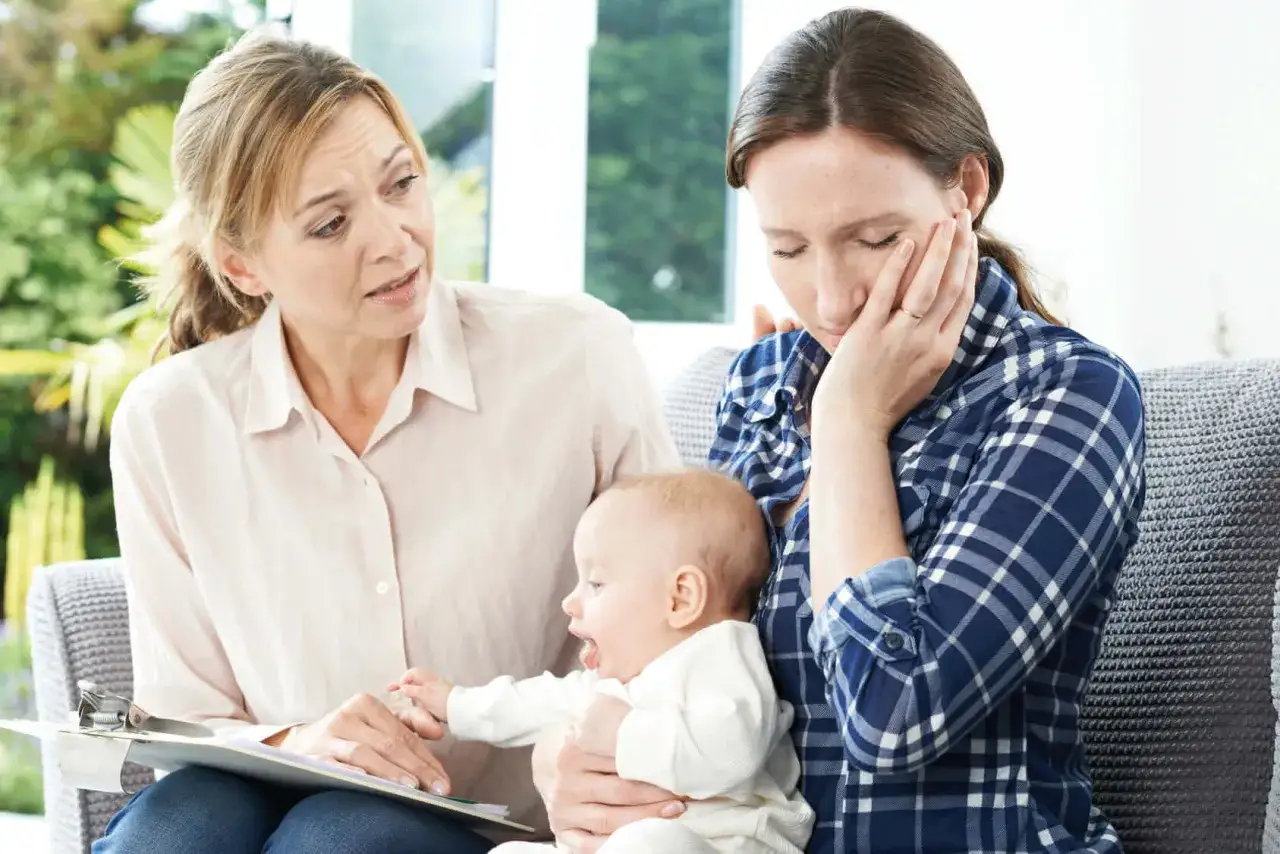 Psychologin spricht mit einer verzweifelten Mutter, die ihr Baby hält. Thema: Kontaktabbruch Geschwister Psychologie.