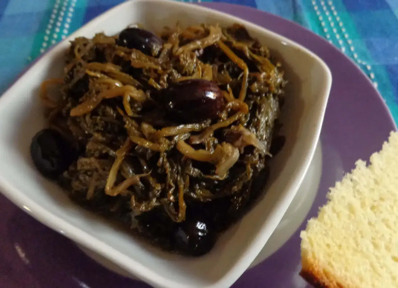 Paparina ricetta: verdura cotta con olive nere in una ciotola bianca, accompagnata da una fetta di pane.