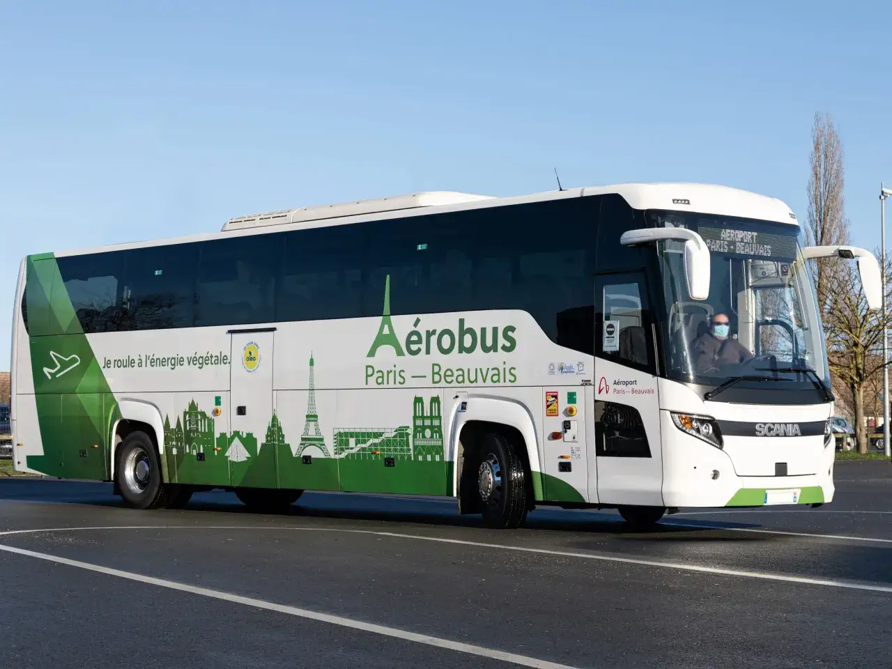 Un bus Aérobus Paris-Beauvais, aux couleurs vertes et blanches, roule sur une route. Il transporte des passagers vers l'aéroport.