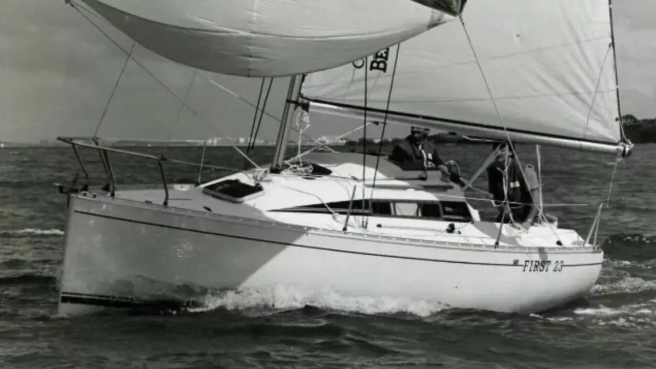 Un voilier First 23 navigue sur une mer agitée, deux personnes à bord profitent de la brise.