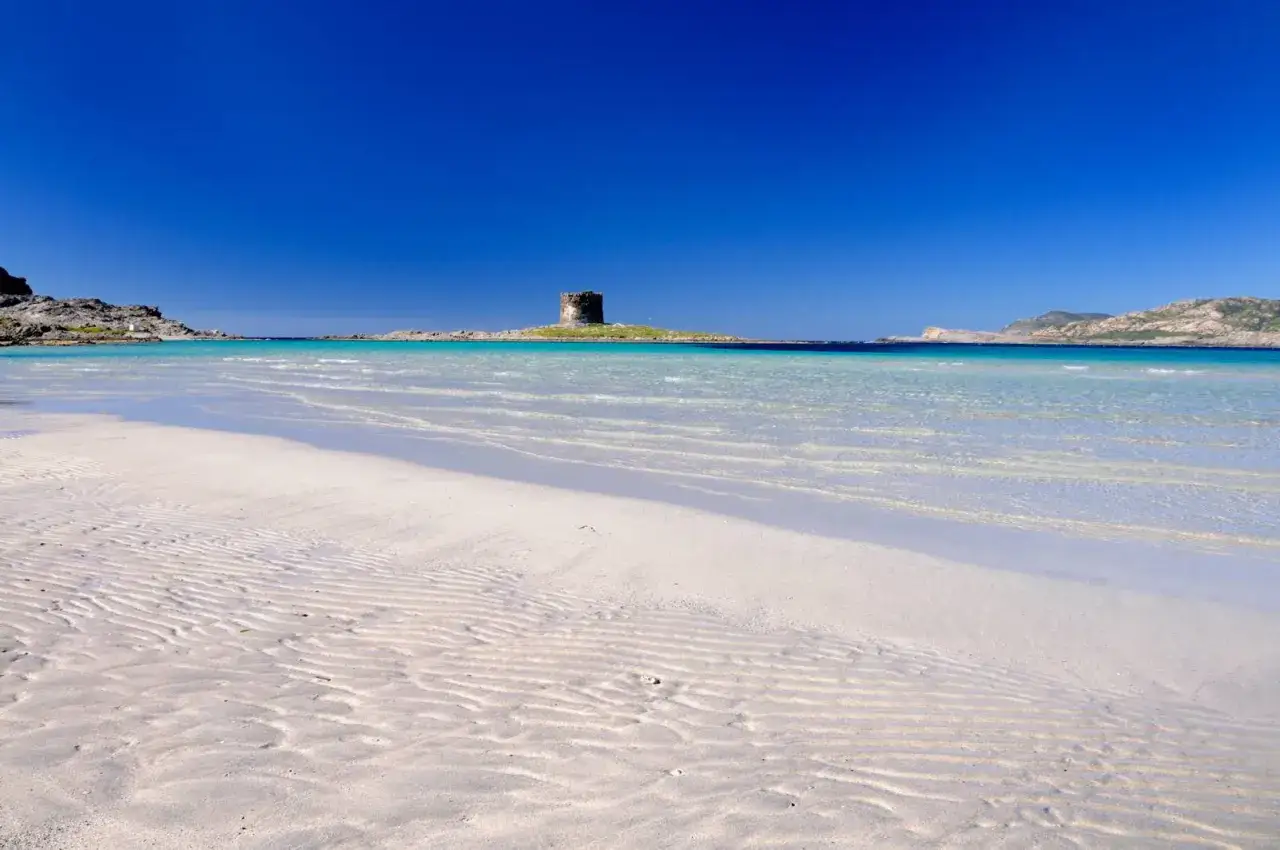 Torre aragonese su isolotto in acque cristalline, una delle spiagge pi&ugrave; belle Sardegna nord. Sabbia bianca e mare turchese.